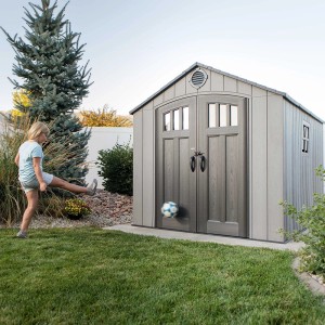 Graues Lifetime Kunststoff-Gartenhaus Jupiter (6,9 m²) mit spielendem Kind und Fußball.