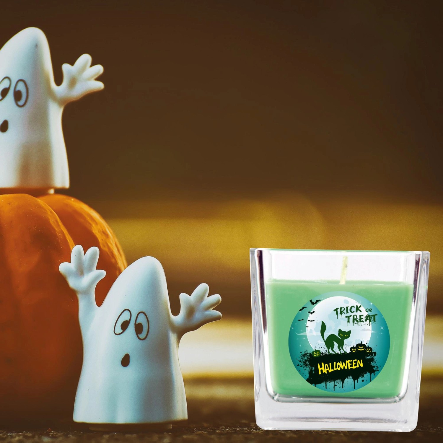 Grüne HS Candle Duftkerze im Glas mit Halloween-Motiv, neben Kürbis und Geistern.