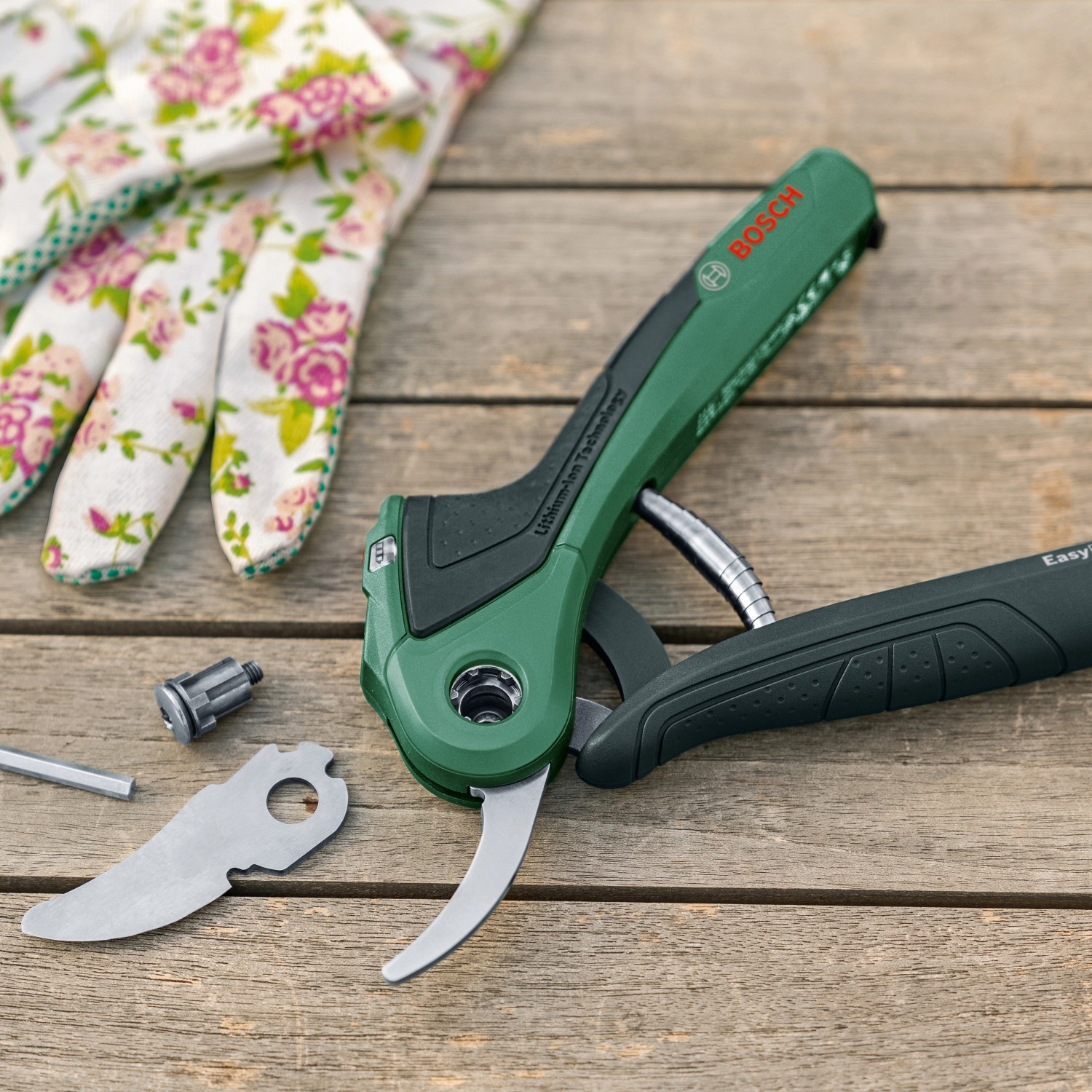 Bosch EasyPrune Akku-Gartenschere mit Zubehör und Gartenhandschuhen auf Holztisch.
