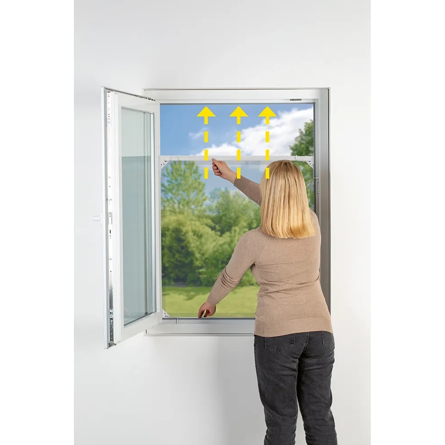 Frau montiert Easymaxx Moskitonetz Magic Fit am Fenster. Ausziehbarer Insektenschutzrahmen in Weiß.
