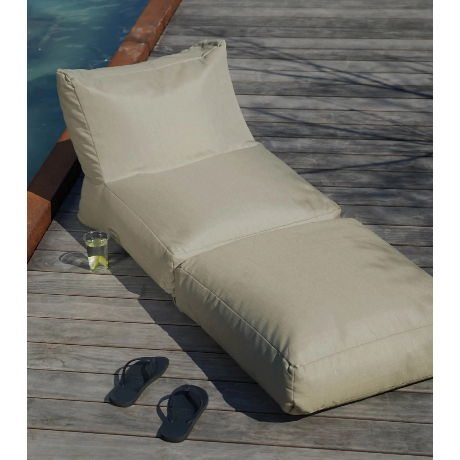 Sandfarbener mokebo Outdoor Sitzsack/Gartenliege auf Holzdeck mit Getränk und Flip-Flops.
