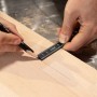 Person misst mit schwarzem 2 Meter Kunststoff-Zollstock ein Holzbrett und markiert es präzise mit Bleistift.