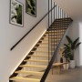 Moderne Holztreppe mit schwarzem Geländer, beleuchtet von warmweißen LED-Streifen unter den Stufen. Paulmann MaxLED Stair Erweiterung.
