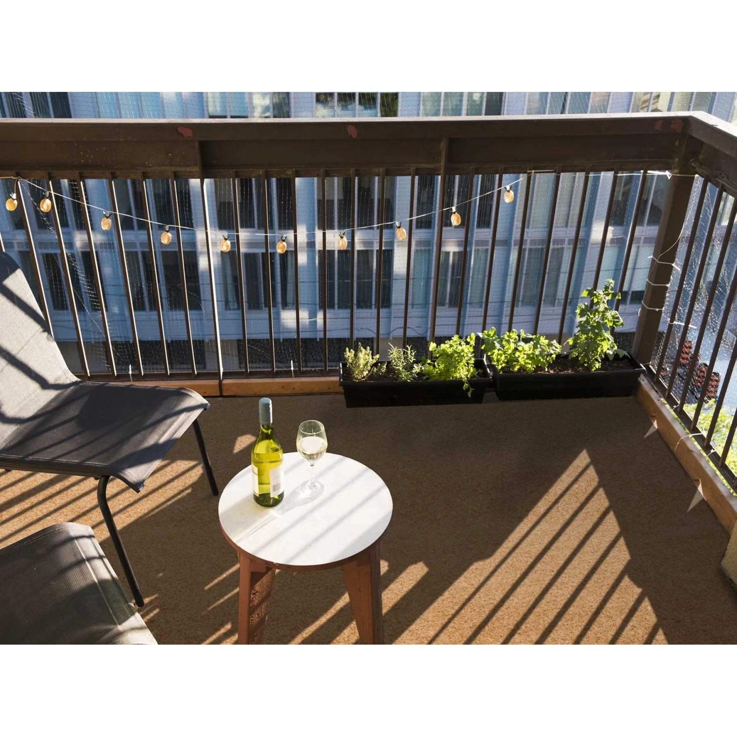 Beiger Primaflor Rasenteppich auf einem Balkon mit Tisch, Stuhl, Wein und Pflanzen.