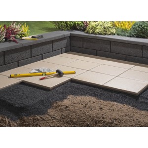 Verlegung von anthrazitfarbenen Gartenmauer-Halbsteinen und Terrassenplatten. Werkzeuge liegen bereit.