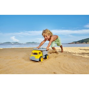 Kind spielt mit gelbem Hape Sandlaster am Strand. Robustes Spielzeug für Sandkasten und mehr.