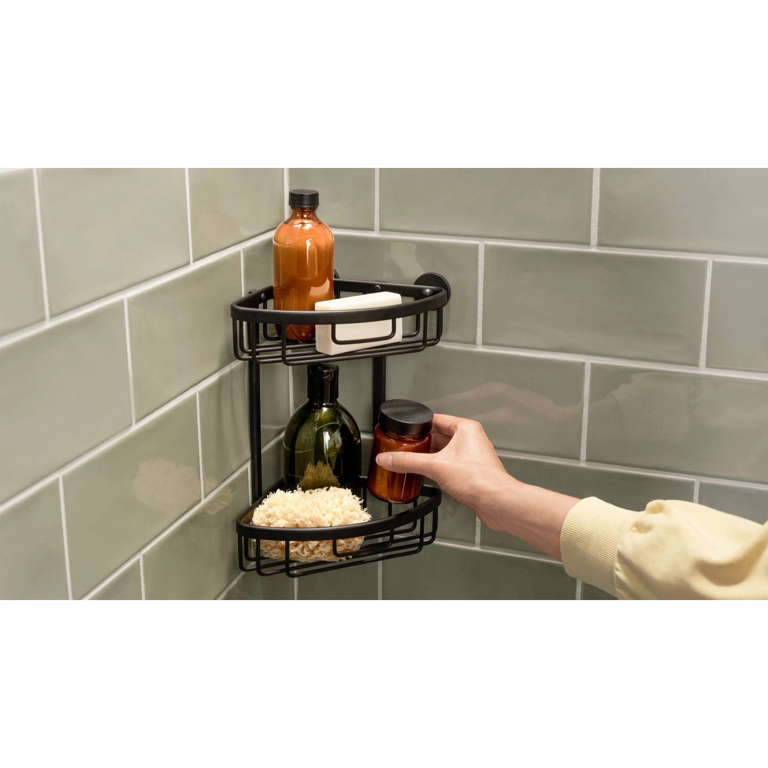 Schwarzer, zweistöckiger Tesa Aluxx Eckduschkorb mit Duschutensilien an grüner Wand.