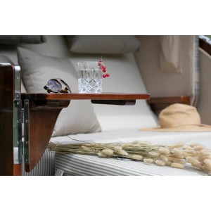 Detailaufnahme: Mahagoni Strandkorb Westerland mit Bullauge, Ablagetisch, Getränk und Dekoration.