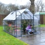 Graues Palram Canopia Gewächshaus 9 m² mit Fundamentrahmen und Person bei der Gartenarbeit.
