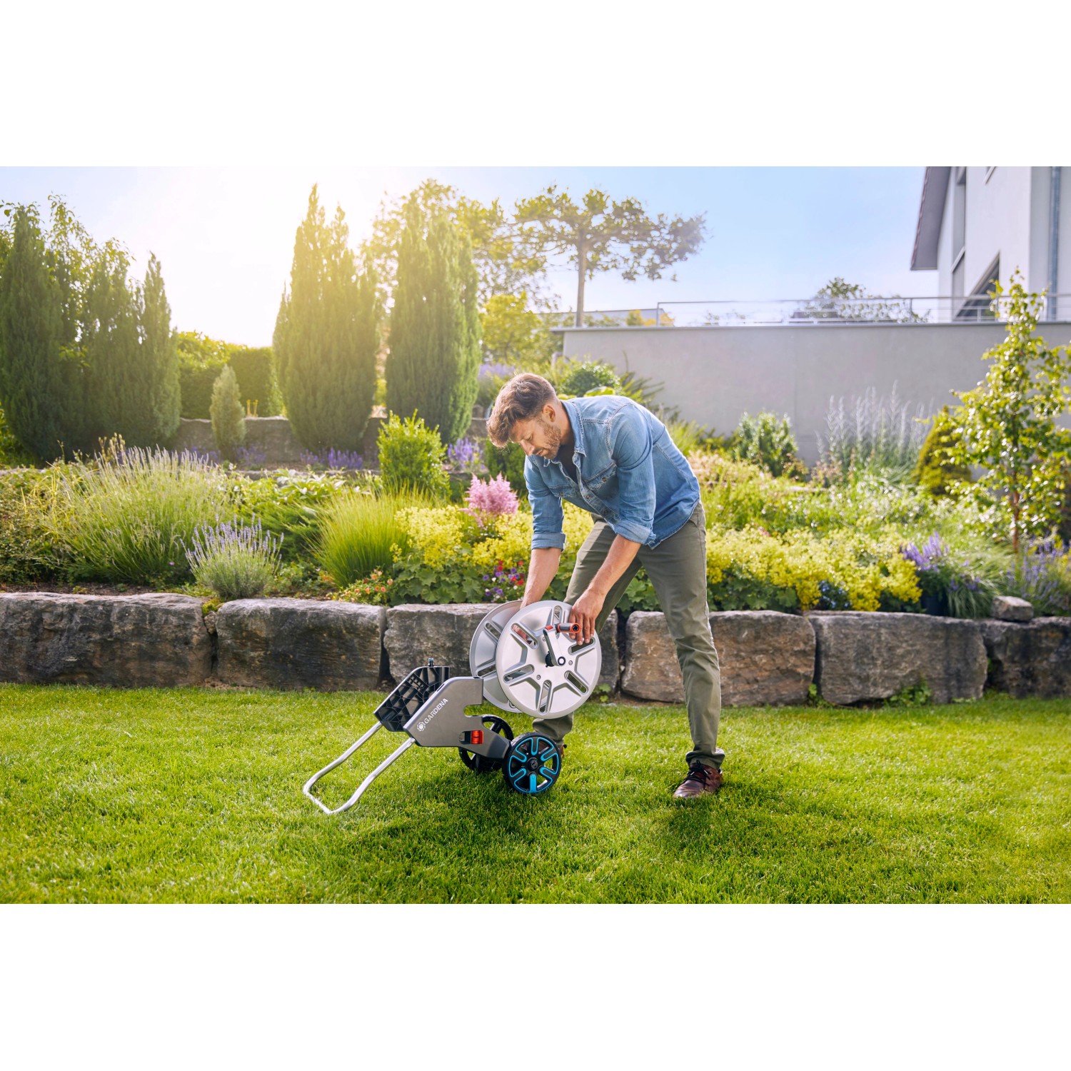 Gardena CleverRoll M Metall Schlauchwagen mit Mann im Garten. Robuste Metalltrommel für bis zu 60m Schlauch.