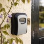 Schlüsselsafe schwarz-grau mit 4-stelligem Zahlencode an heller Hauswand, Wandmontage. Sicherer Schlüsseltresor.