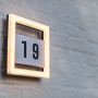 Quadratische LED Hausnummernleuchte Alice mit Rahmen und Ziffernblatt, montiert an einer Wand.