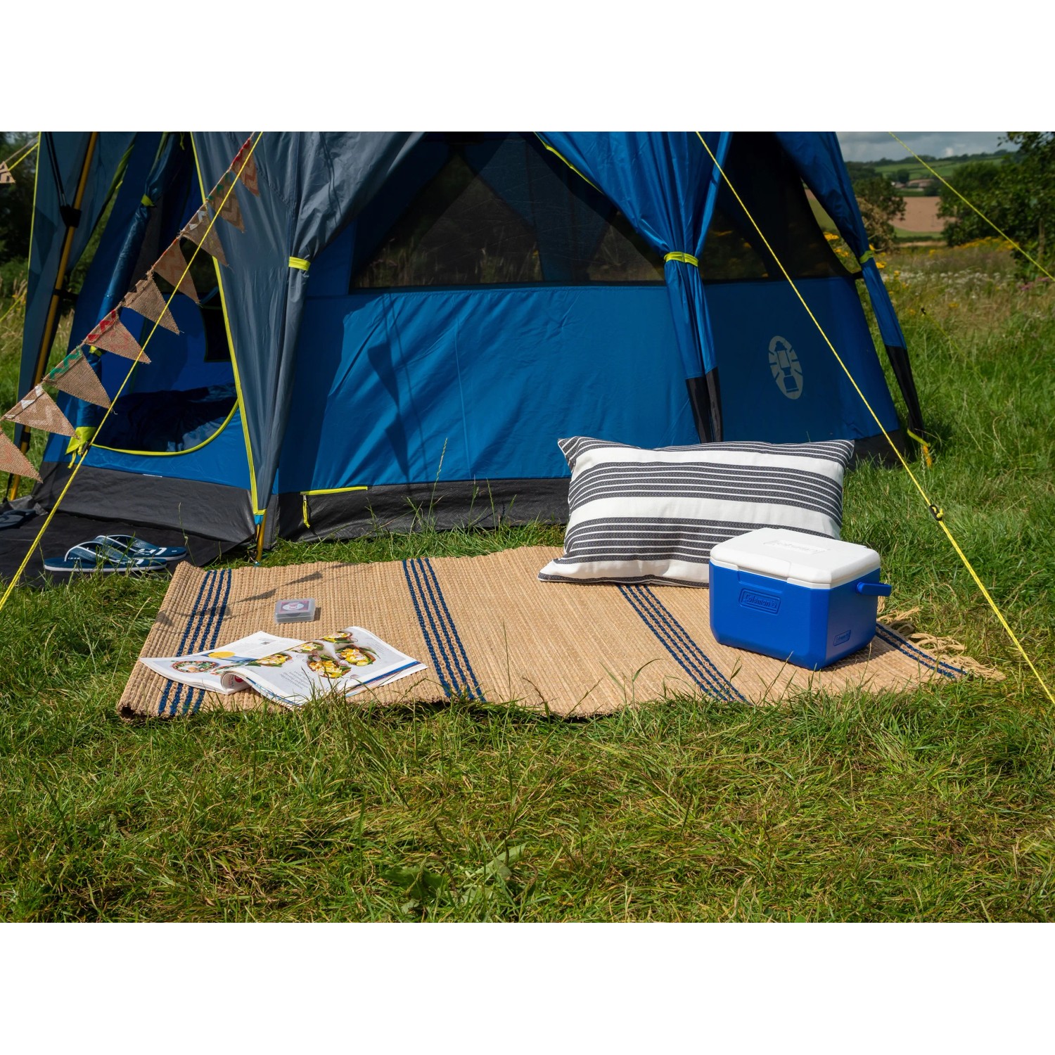 Campingaz Kühlbox 5QT blau-weiß neben Kissen und Zelt auf Rasen.