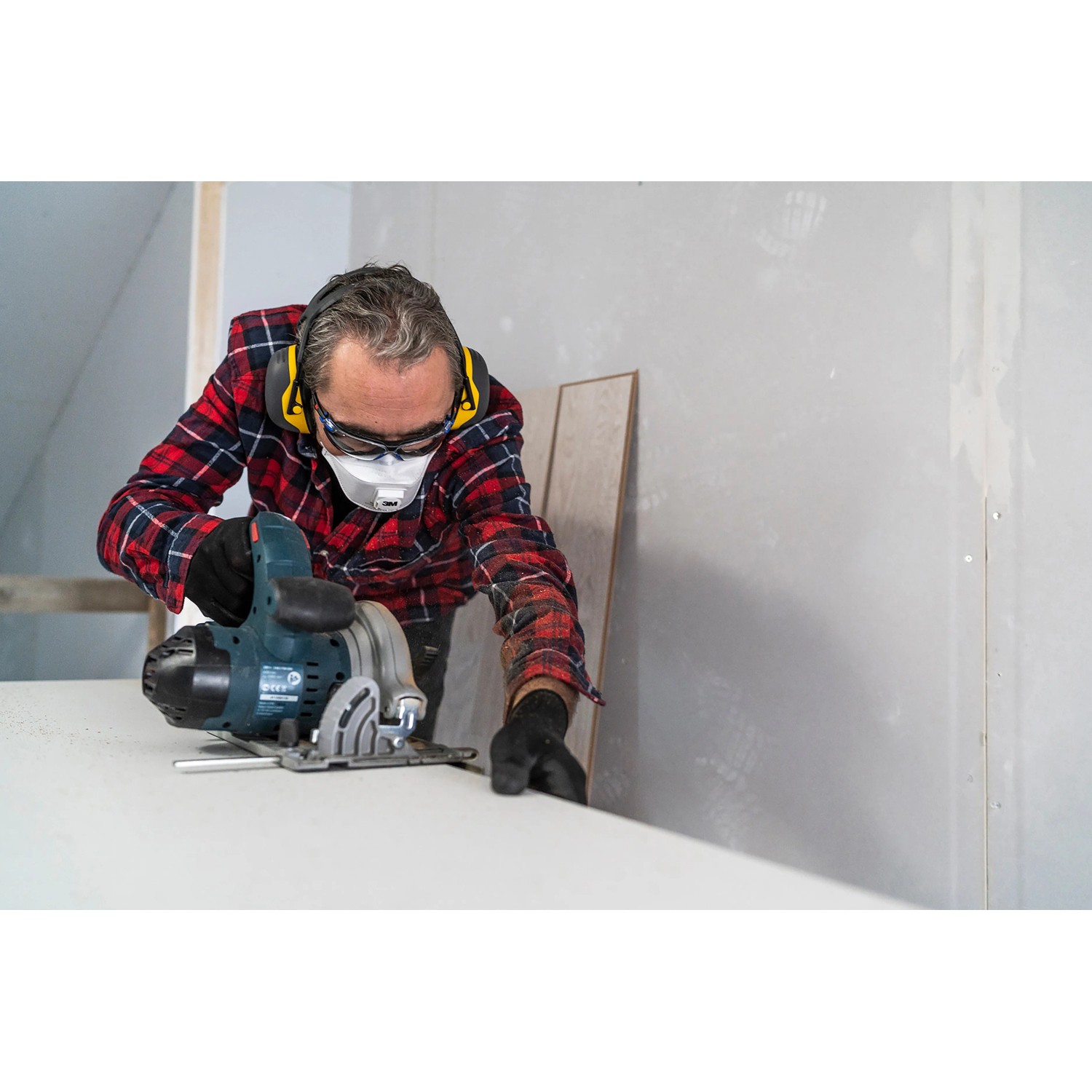 Handwerker mit 3M Peltor Gehörschutz X2A beim Sägen, effektiver Kapselgehörschutz für Heimwerker.