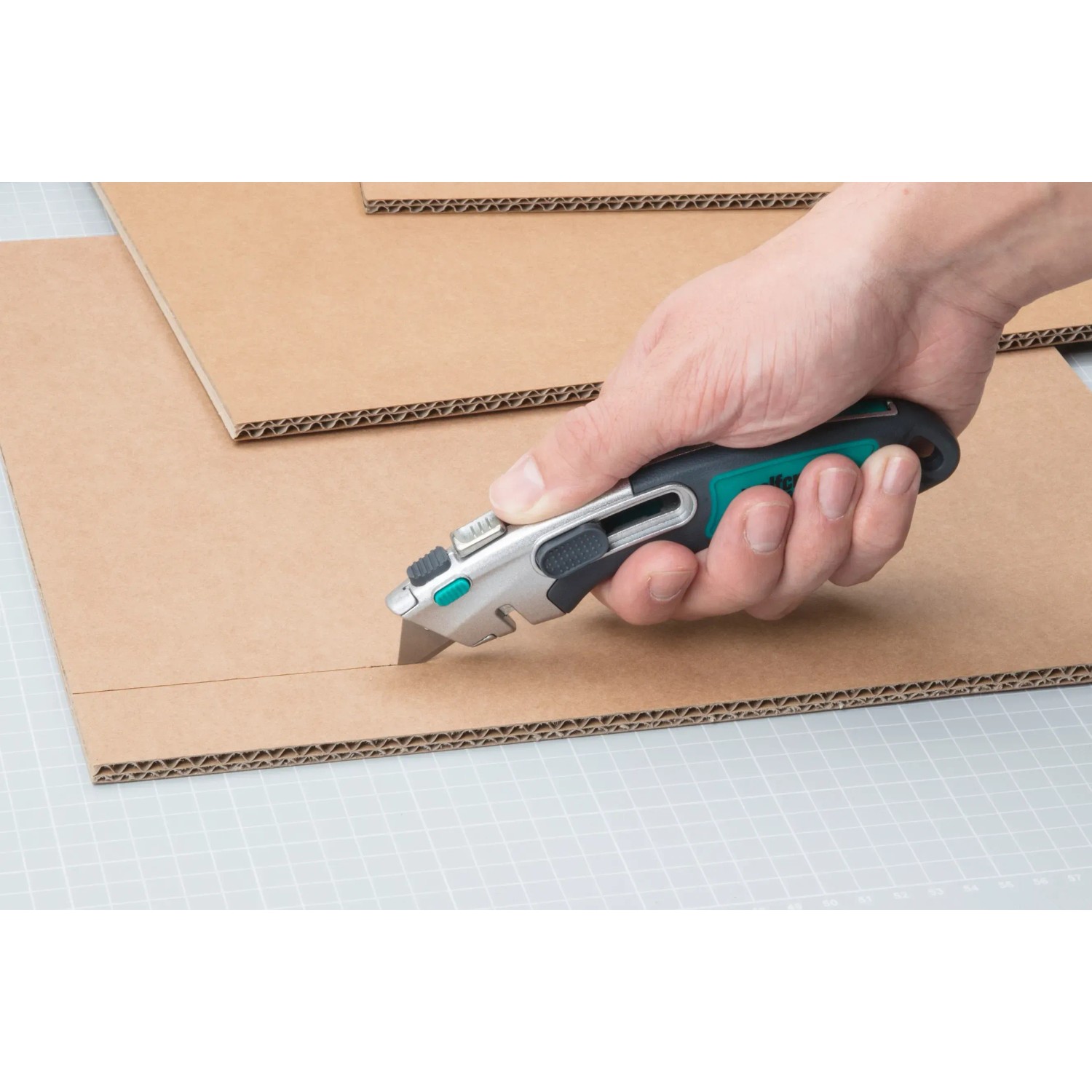 Hand schneidet Pappe mit wolfcraft Profi-Dual-Sicherheitsmesser (Trapezklinge).