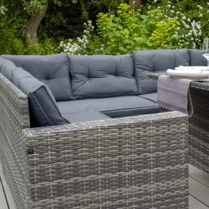 Graues Polyrattan Gartenmöbel Set mit Ecksofa, Tisch und Hockern mit grauen Kissen.