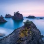 Komar Fototapete Vlies Secret Beach: Küstenlandschaft mit Felsen im Wasser bei Sonnenuntergang.