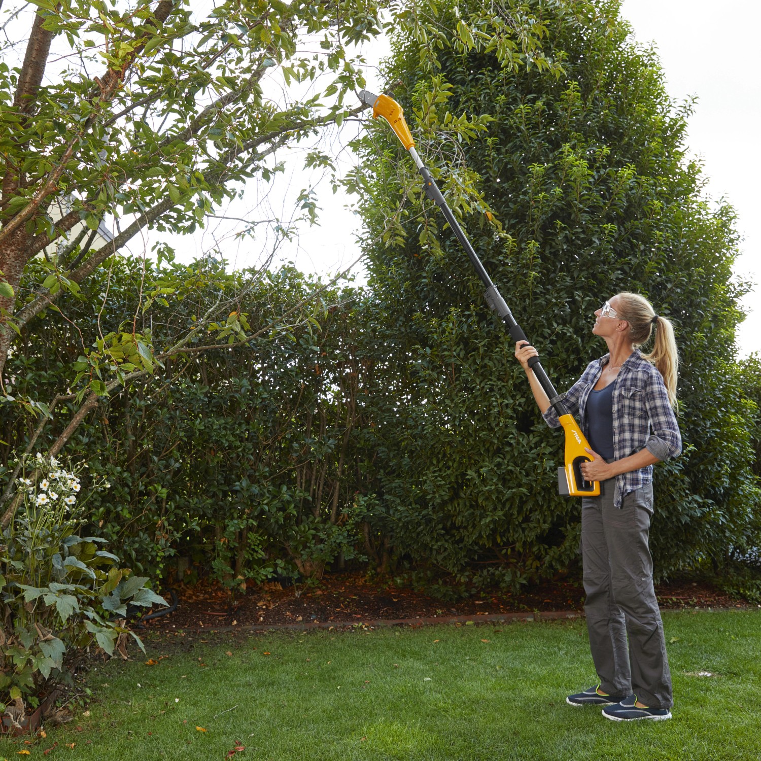Frau schneidet Baum mit Stiga Akku-Multitool MT 100e Akku-Hochentaster im Garten.