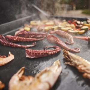 Weber Slate GPD 76cm Plancha Gasgrill mit Oktopus, Garnelen und Gemüse auf Grillfläche.