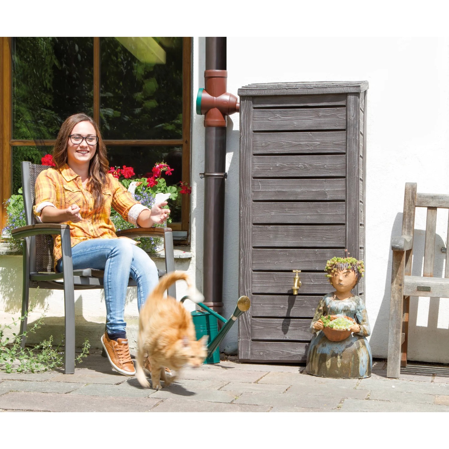 Arves Regentonne Norway 230 l dunkelbraun im Garten mit Frau, Katze und Dekoration.