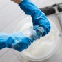 Hände mit blauen Mehrweghandschuhen Robust Größe S wringen einen Schwamm in einem Eimer mit Seifenlauge aus.