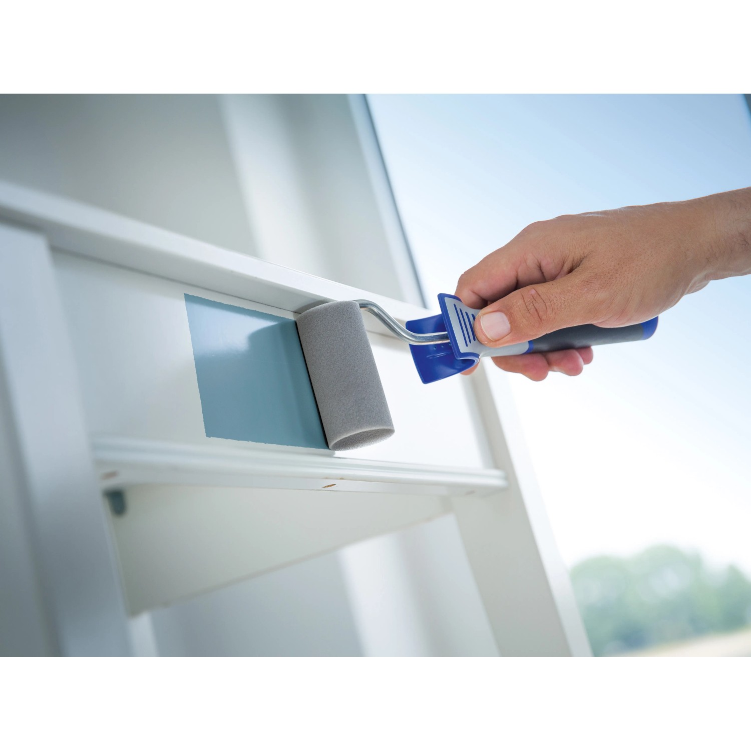 Hand mit LUX Schaumroller (7 cm) beim Lackieren eines Fensterrahmens.