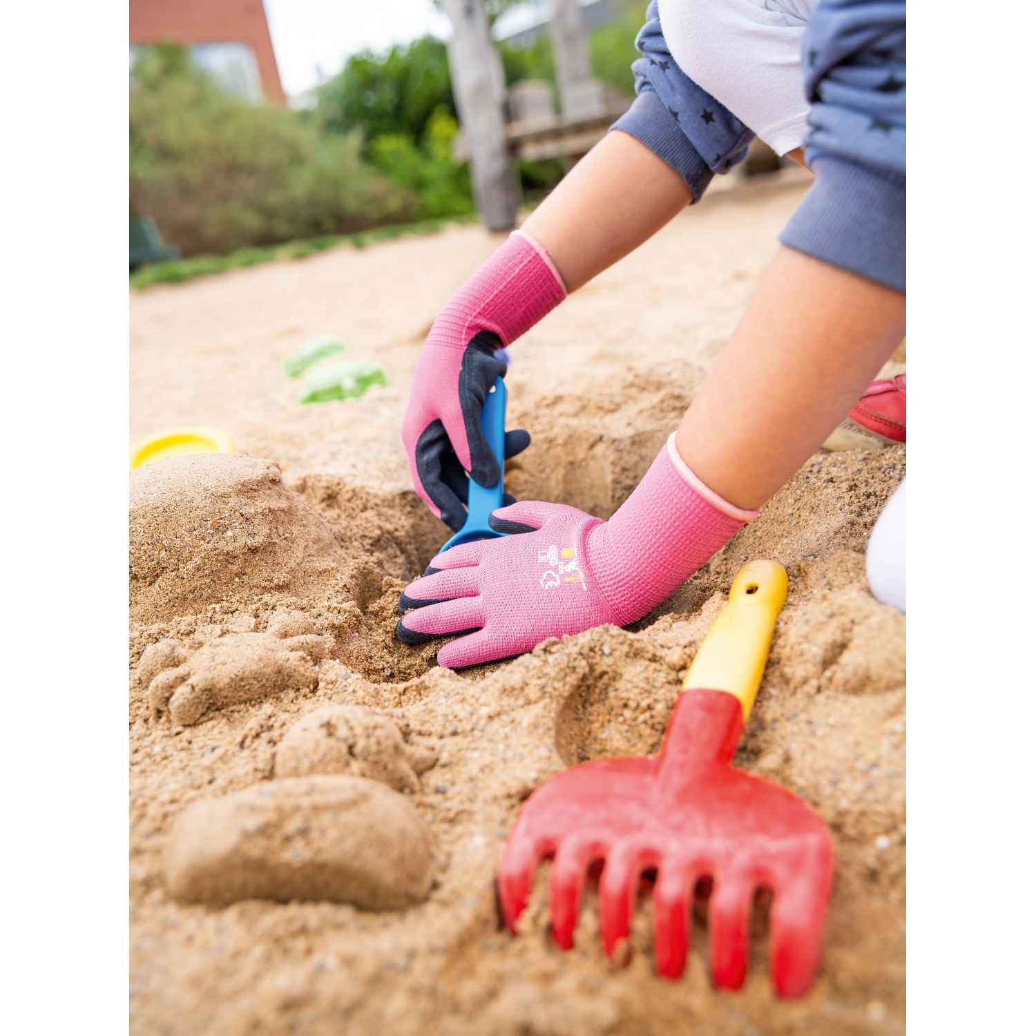 Kind mit pinken Gartenhandschuhen (Größe 4) mit Naturlatex-Beschichtung beim Spielen im Sandkasten.