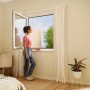 Frau am Fenster mit anthrazitfarbenem tesa® Insect Stop Fliegengitter Premium. Effektiver Insektenschutz.