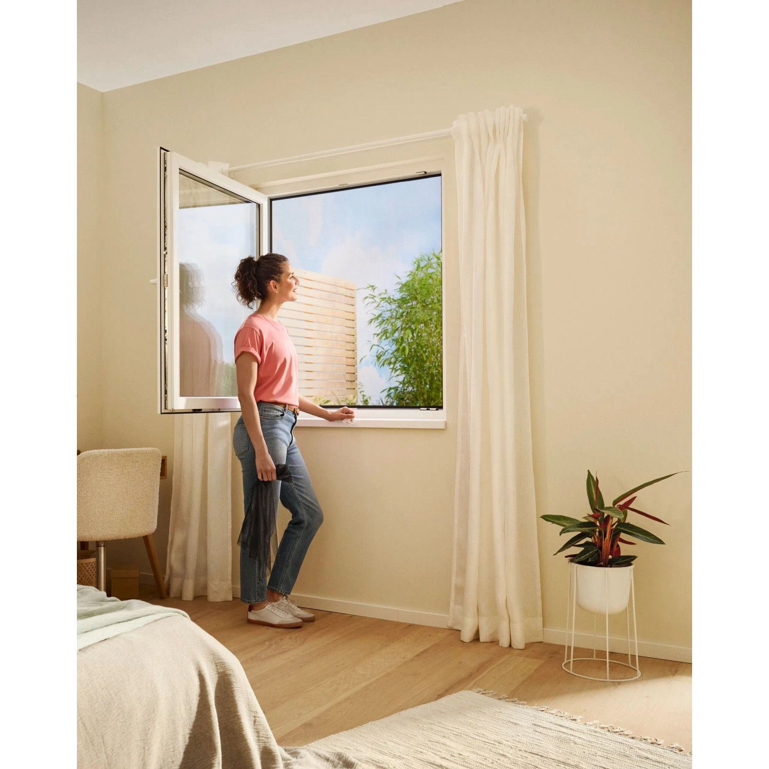 Frau am Fenster mit anthrazitfarbenem tesa® Insect Stop Fliegengitter Premium. Effektiver Insektenschutz.