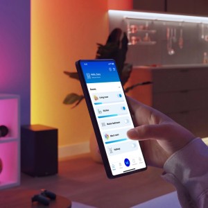 Hand steuert Philips Smart-LED-Leuchtmittel E14 über App. Smartphone zeigt Raumauswahl für smarte Beleuchtung in modernem Raum.