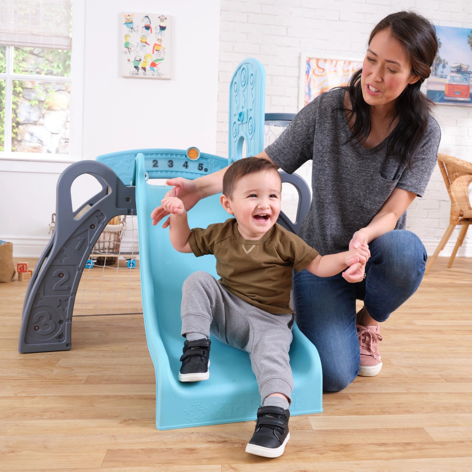 Fröhliches Kleinkind rutscht auf blauer KidKraft Kinderrutsche, Erwachsene hilft. Indoor Spielanlage für Kinder.