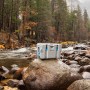Graue Lifetime Kühlbox (73L) mit blauen Akzenten auf einem Felsen am Fluss.