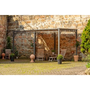 Schwarze Eleo Metall Pergola Sardegna, pulverbeschichtet, mit Sitzgruppe vor Steinwand.