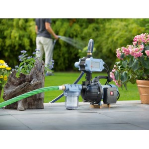 Hauswasserautomat 800 W im Einsatz zur Gartenbewässerung. Pumpe mit Schlauch und Blumen im Hintergrund.