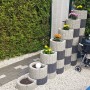Gestapelte anthrazitfarbene Pflanzringe Klein 35x20 cm mit Blumen und Grill im Garten.