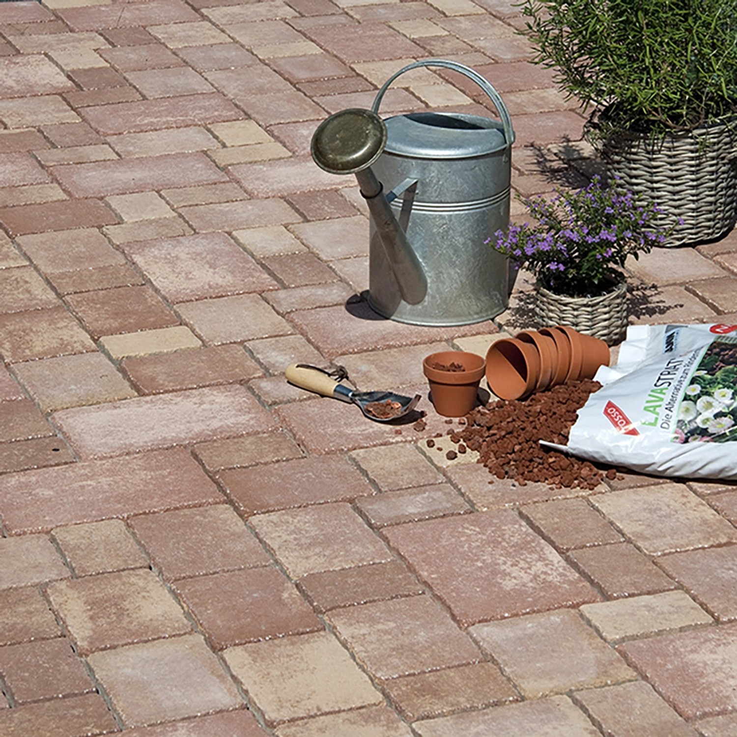 Verlegte, lehmfarbene Mehrformat-Pflastersteine Encanto Beton Antik Terra mit Gießkanne und Gartenzubehör.