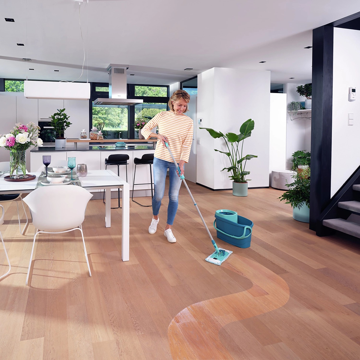 Frau wischt Holzboden mit Leifheit Clean Twist M Ergo Bodenwischer-Set, Eimer und 2 Wischbezügen.