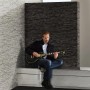 A.S. Création Tapete Stein-Optik grau/schwarz im Raum mit Mann und Gitarre.