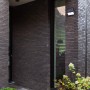 Schwarze Lutec LED Solar-Wandleuchte Tuda mit Bewegungsmelder an dunkler Hauswand.