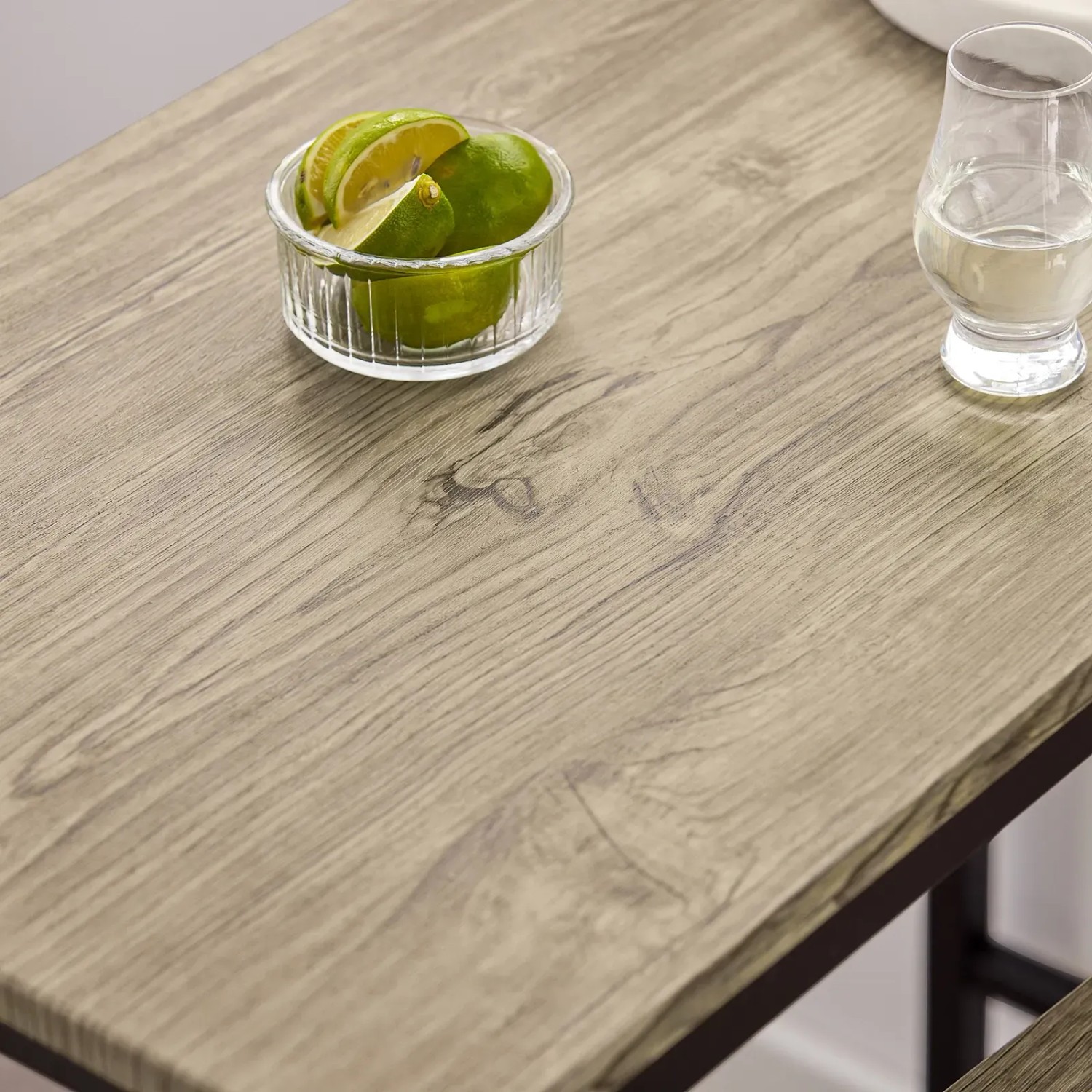 Detailansicht: Bartisch-Set mit Holzplatte in Natur, schwarzes Metallgestell, Limetten und Wasserglas.