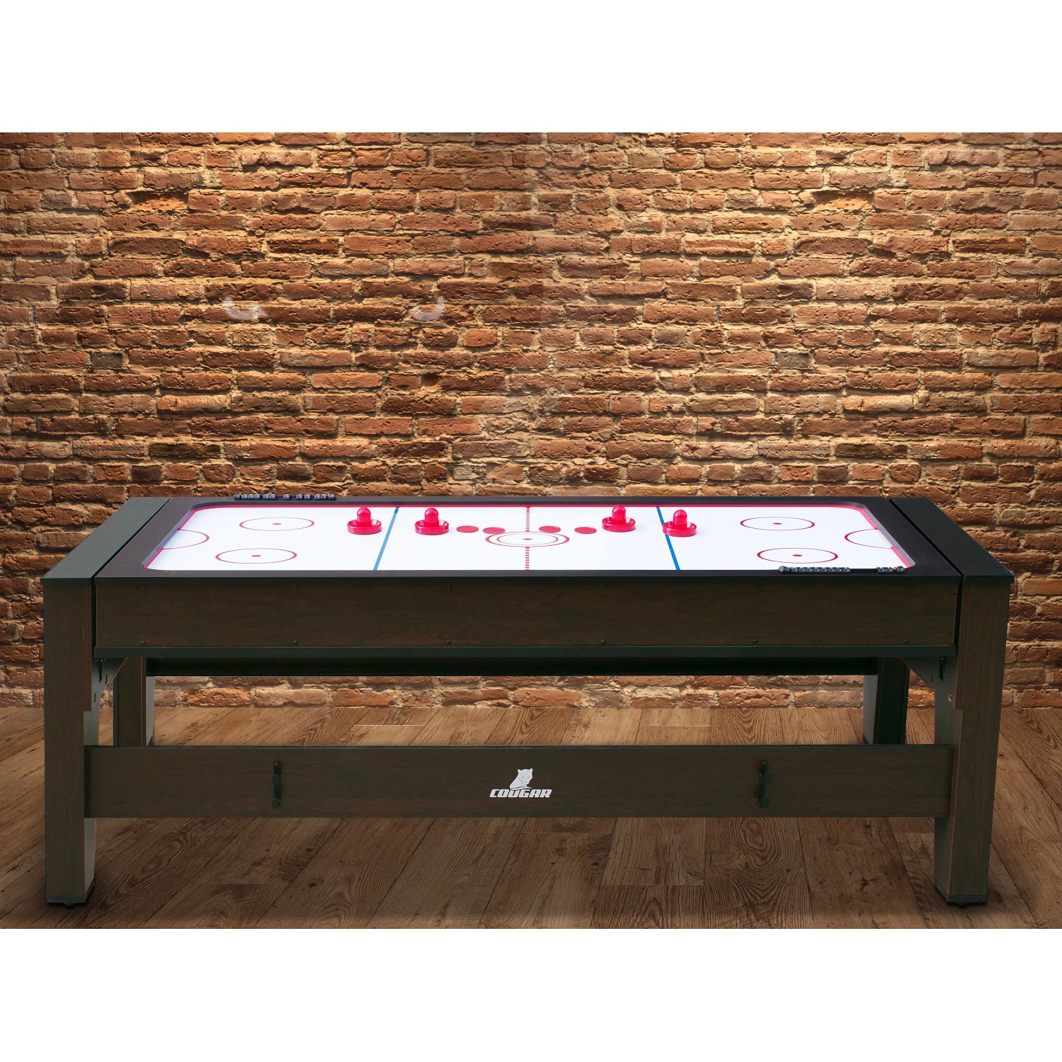 Reverso Spieltisch als Airhockey-Tisch mit roten Pucks vor Backsteinwand.