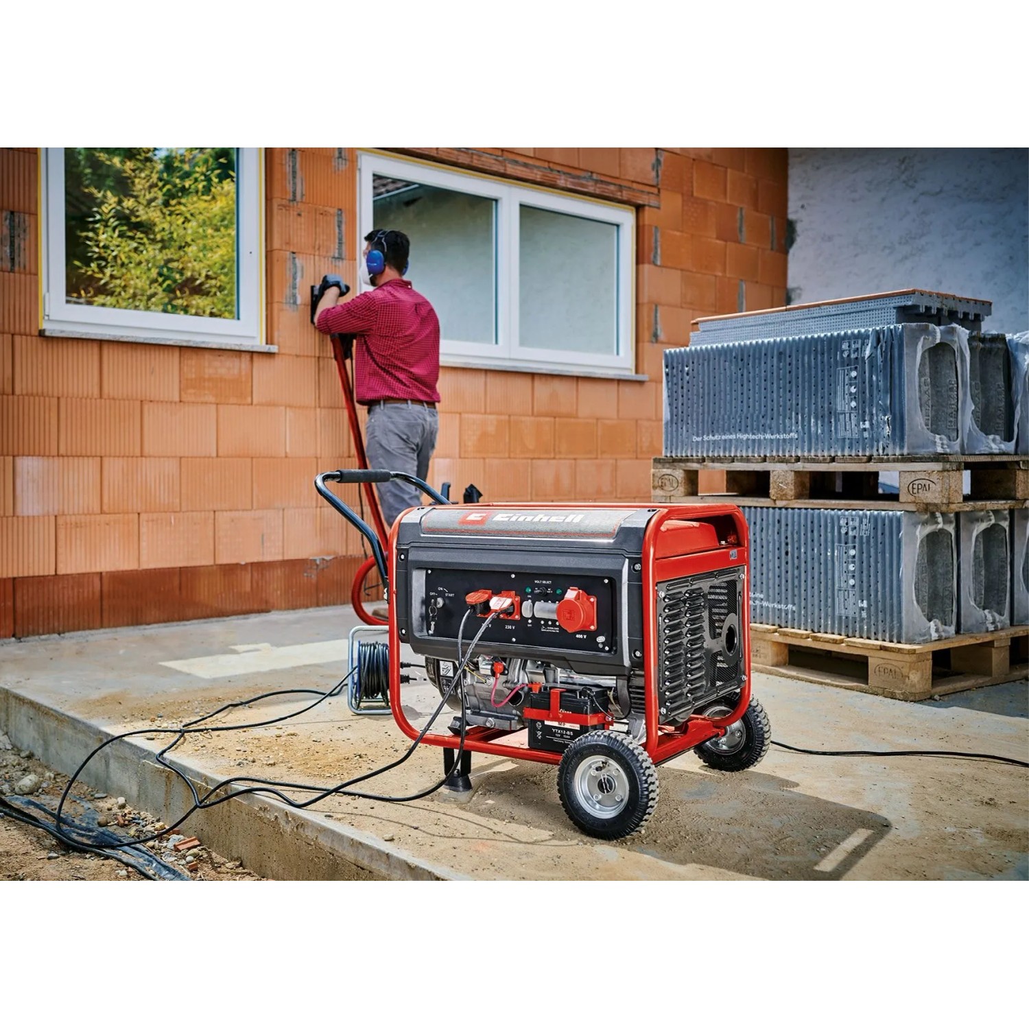 Roter, robuster Einhell Benzin-Stromerzeuger TC-PG 65/E5 auf Rädern versorgt Werkzeug auf Baustelle.