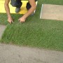 Verlegen von Spiel- und Sport-Rollrasen: Person verlegt Rasenstück. Strapazierfähiger Rasen für den Garten.