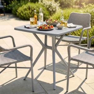 Grauer, eckiger CLP Gartentisch Becky aus Kunststoff auf einer Terrasse, gedeckt mit Essen und Getränken, umgeben von Stühlen.