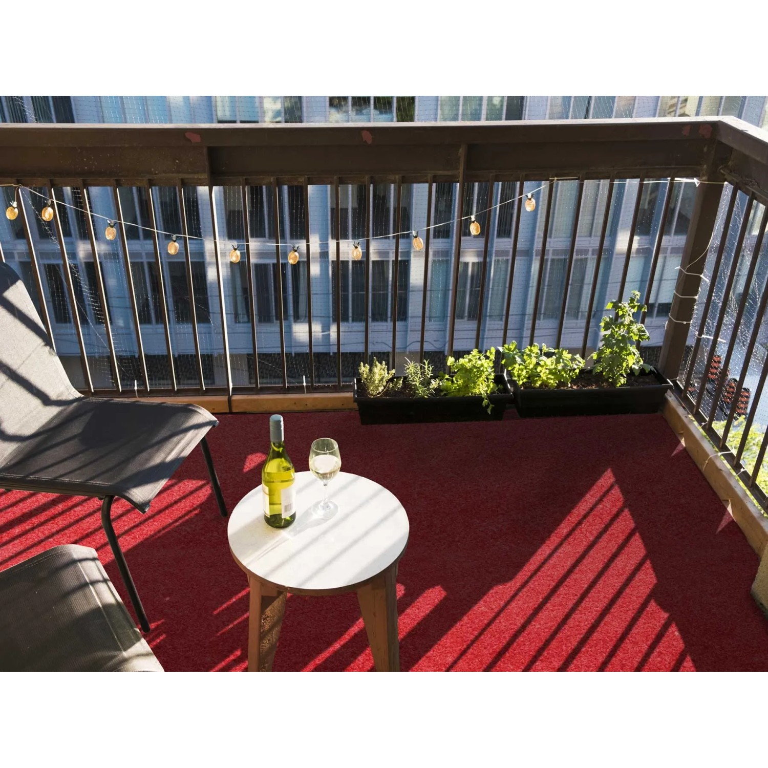 Rot gemusterter Primaflor Rasenteppich auf einem Balkon mit Tisch und Stuhl.