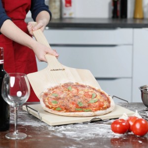 Person schiebt frische Pizza mit großem Relaxdays Pizzaschieber aus Kiefernholz auf Pizzastein in der Küche.