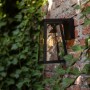 Anthrazitfarbene Lutec LED Solar-Wandleuchte Fia an einer Backsteinmauer mit Efeu.
