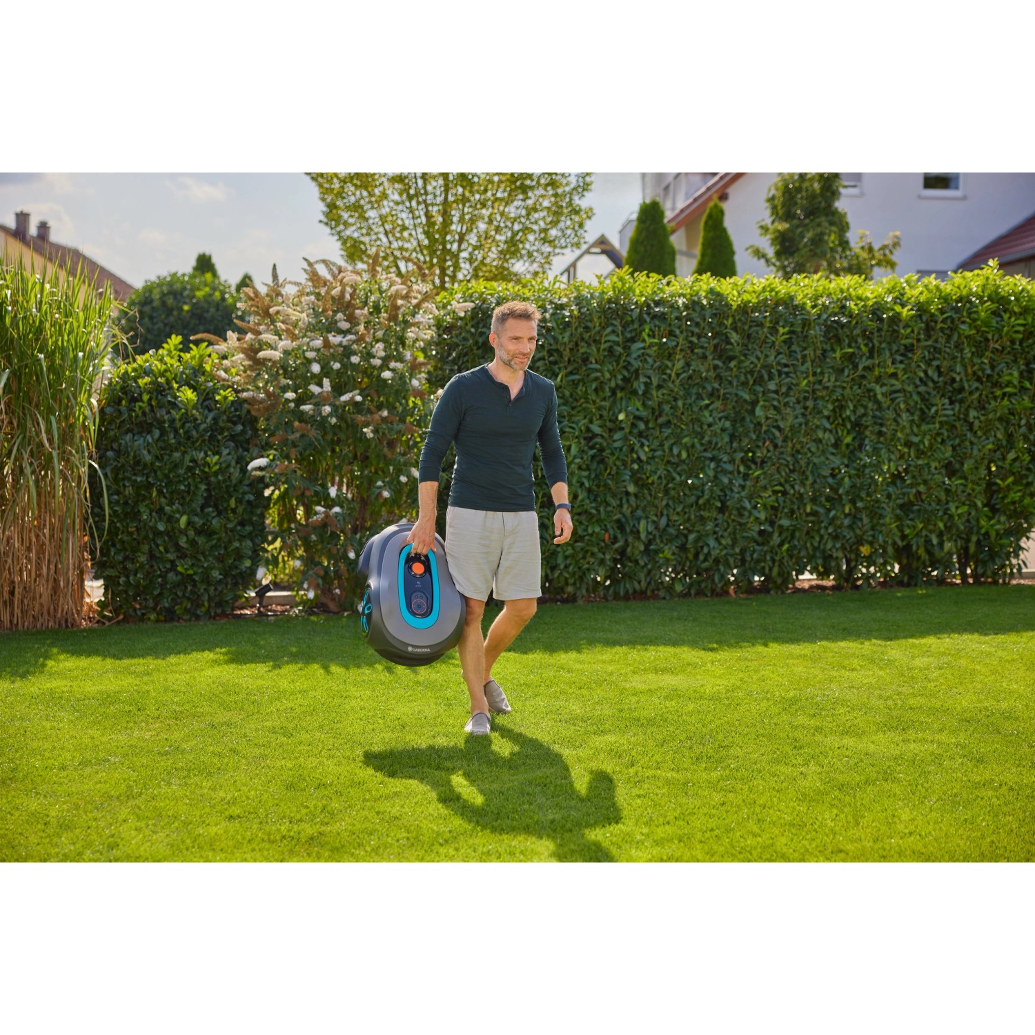 Mann trägt Gardena Mähroboter Smart Sileno Max 1.500 m² über Rasenfläche.