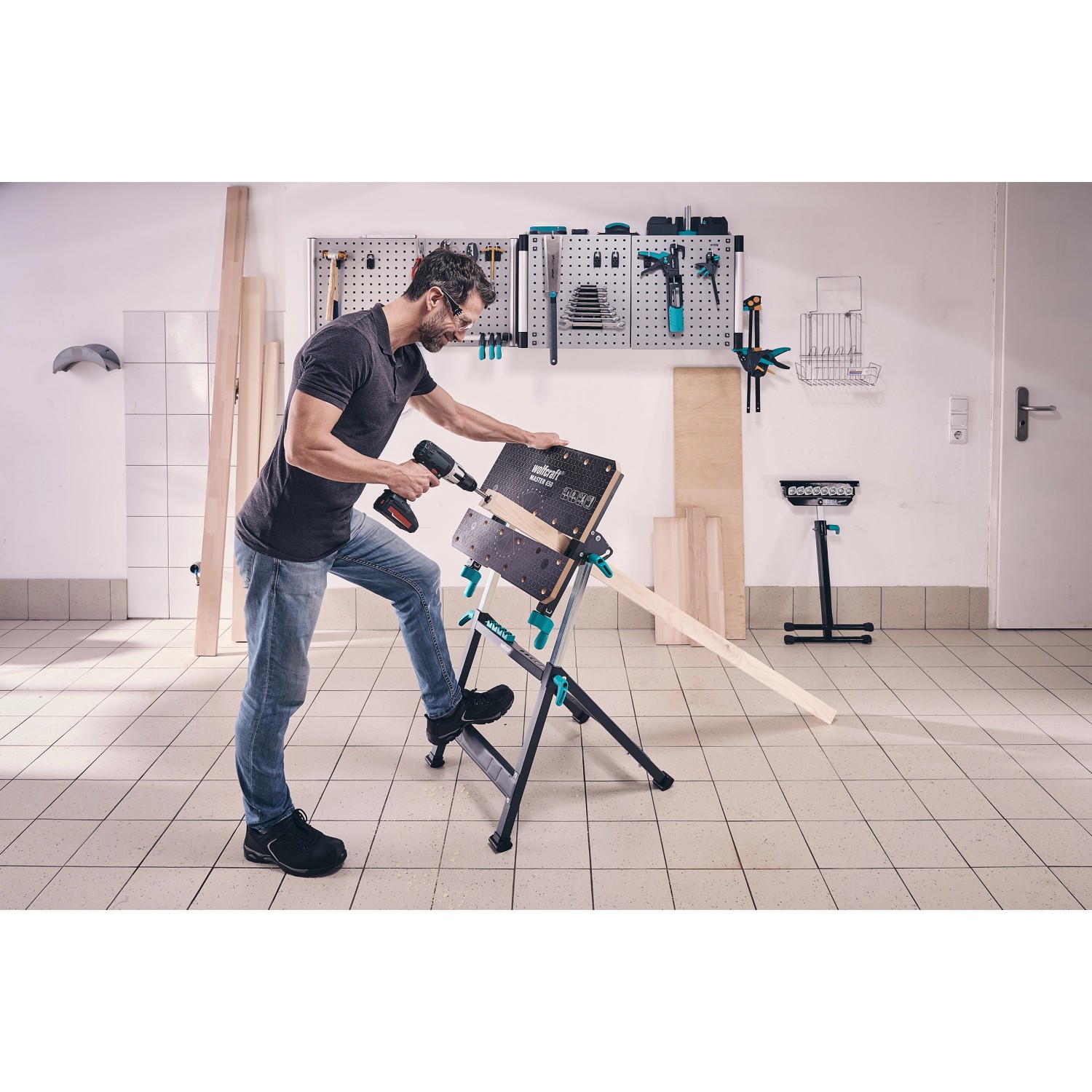 Wolfcraft Master 650 Ergo Werkbank im Einsatz: Mann bohrt Loch in Holz. Höhenverstellbar, mobil.