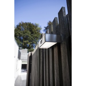 Moderne, eckige Lutec LED Solar-Wandleuchte Brick aus Edelstahl an Holzzaun.